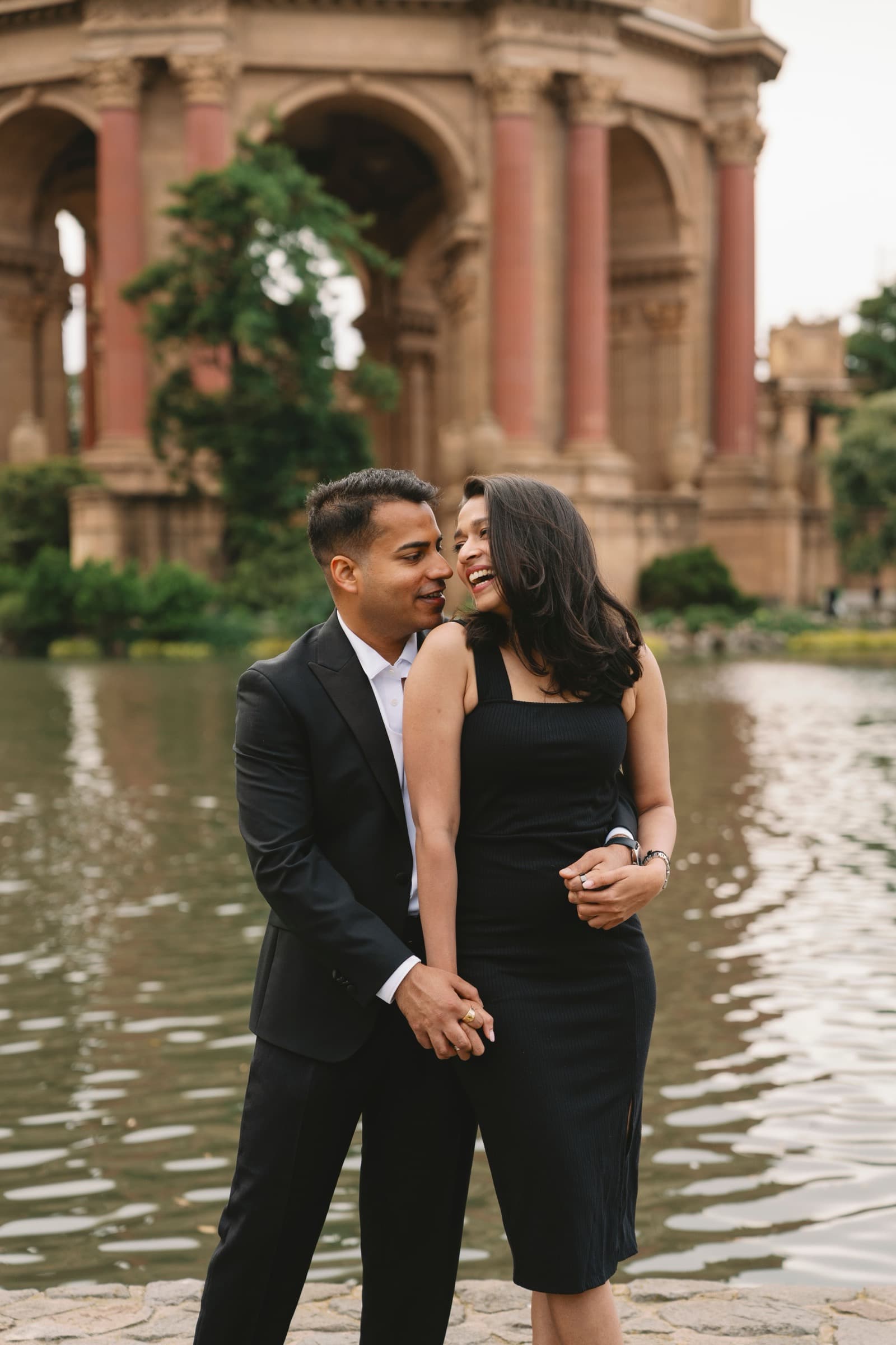 Devanshi and Shantanu laughing together by the lagoon at the Palace of Fine Arts